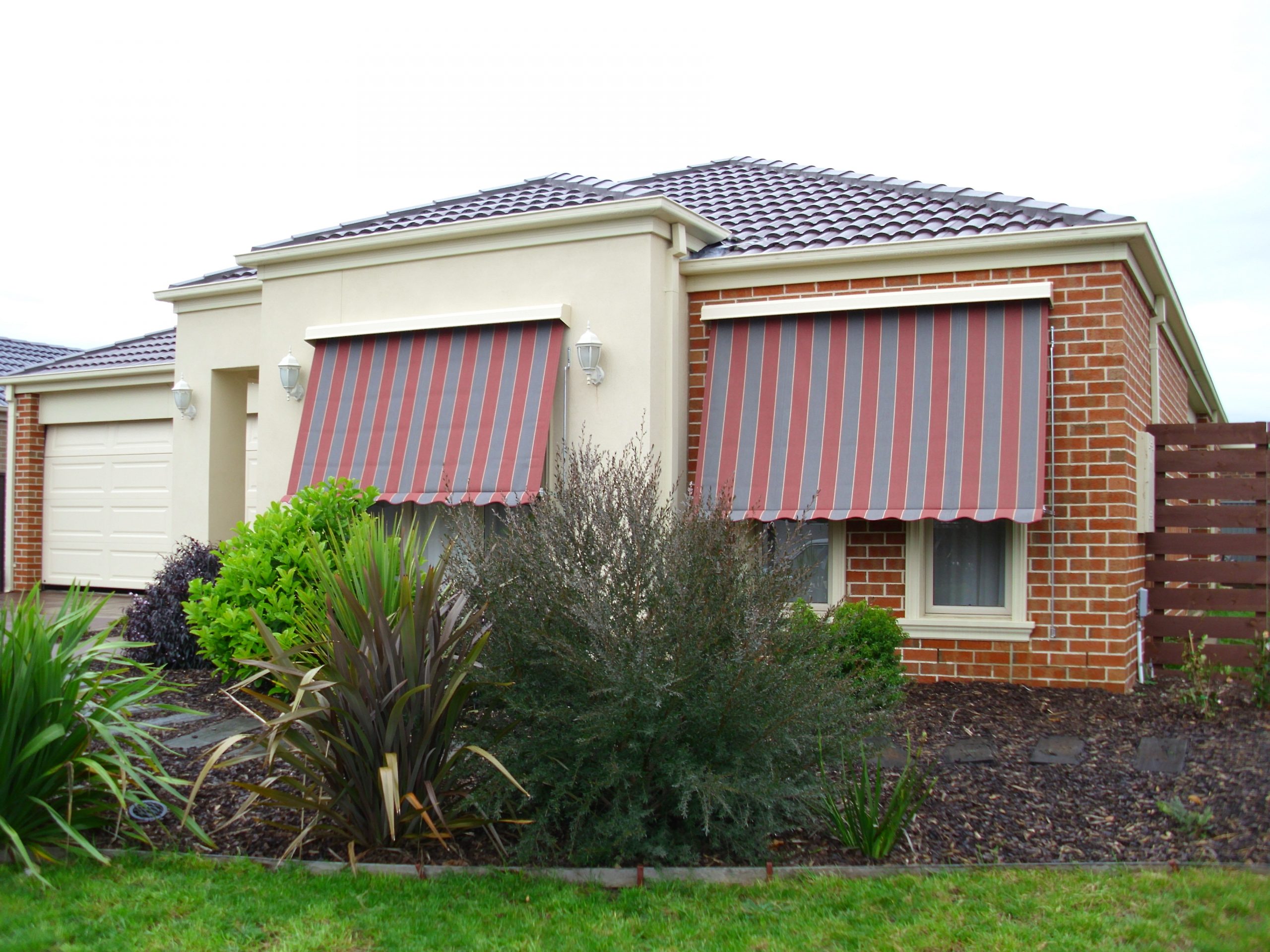 Modern home featuring custom red and grey striped retractable window awnings for sun protection