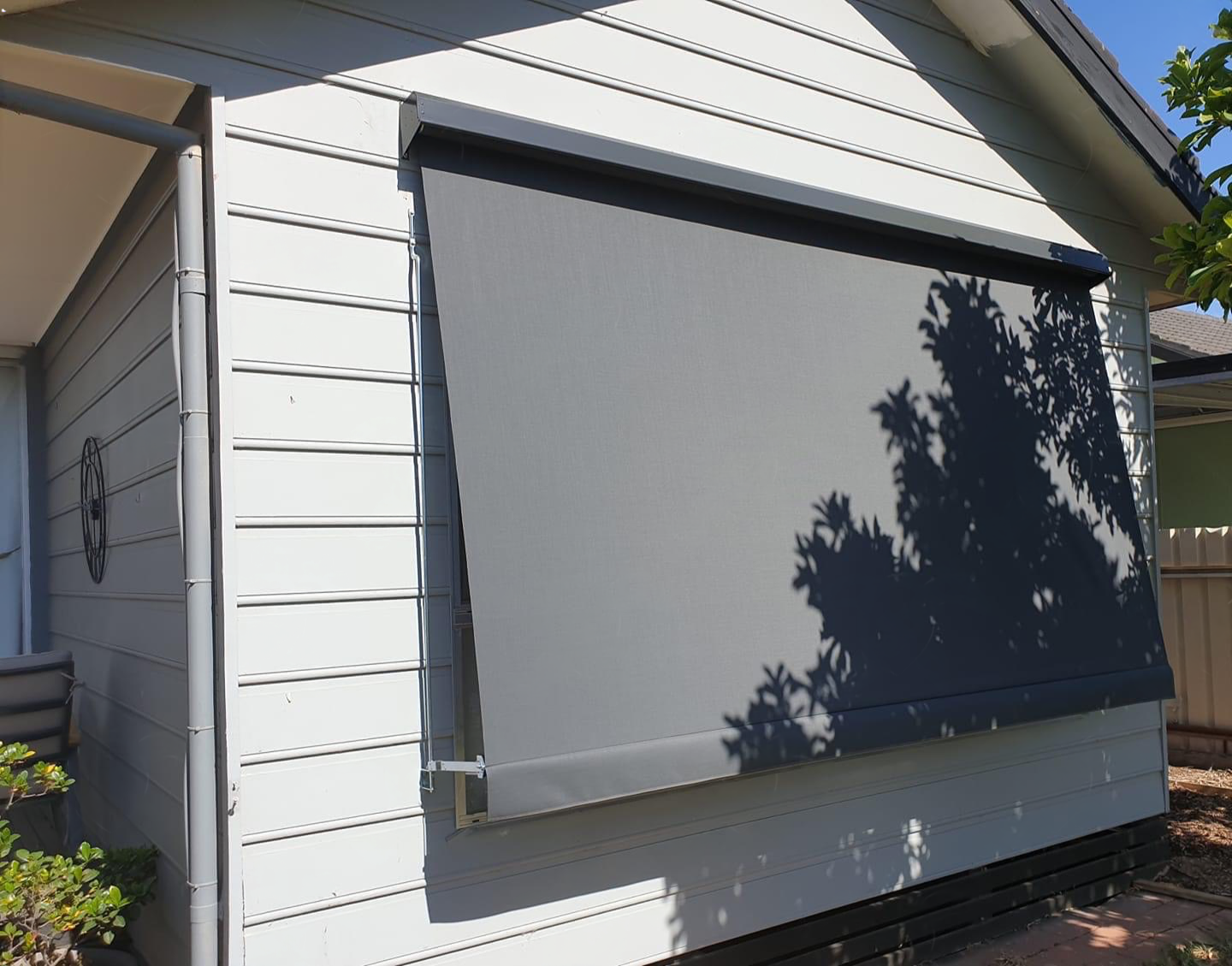 Grey straight-drop outdoor awning blind installed on a white house window